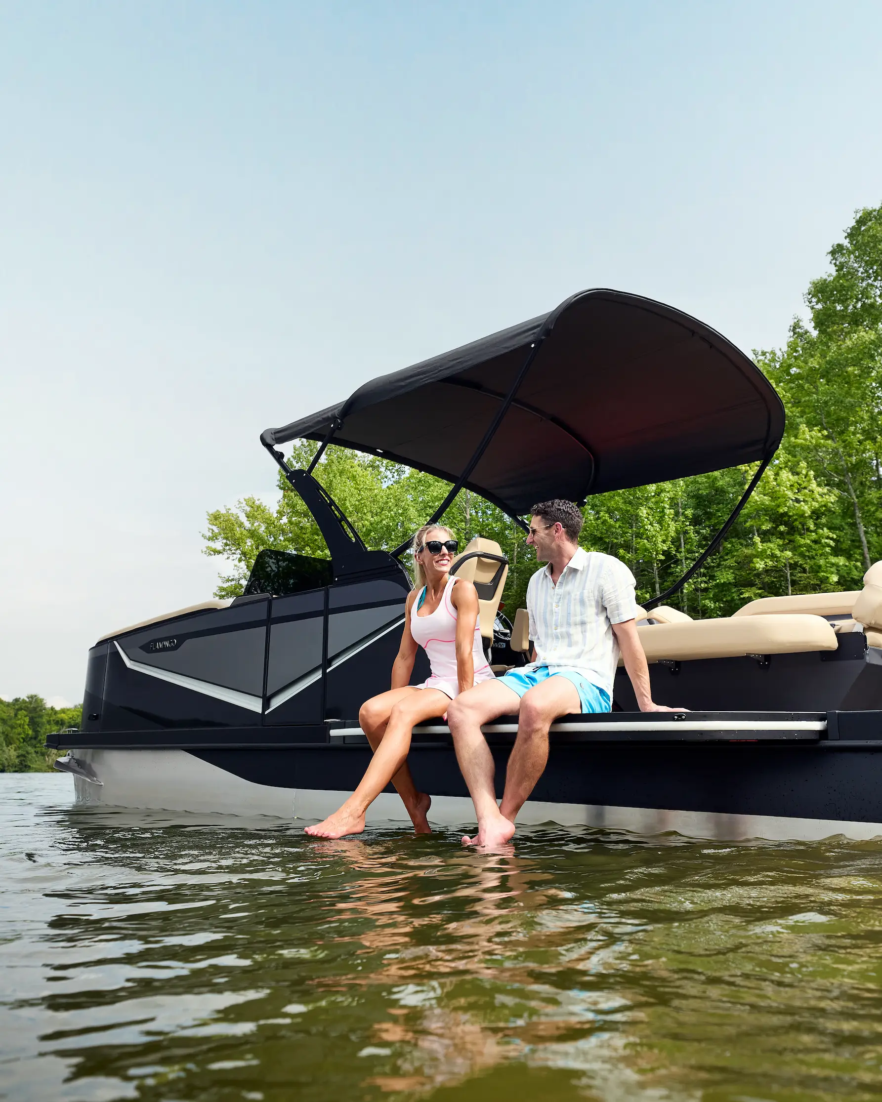 A couple relaxing on the edge of the ROVE, feet in the water under the bimini